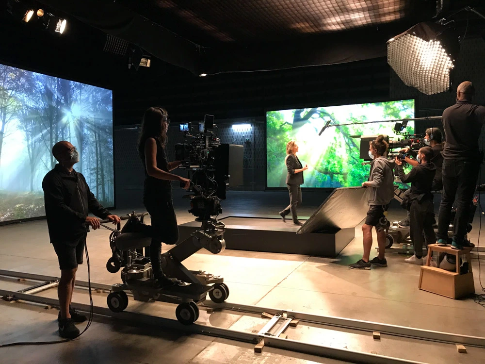 Glassy Films crew on a camera dolly in a virtual production studio with forest LED screens
