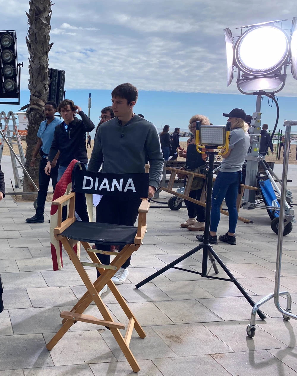 Actor next to a director's chair on a Glassy Films seafront set, with crew and lights