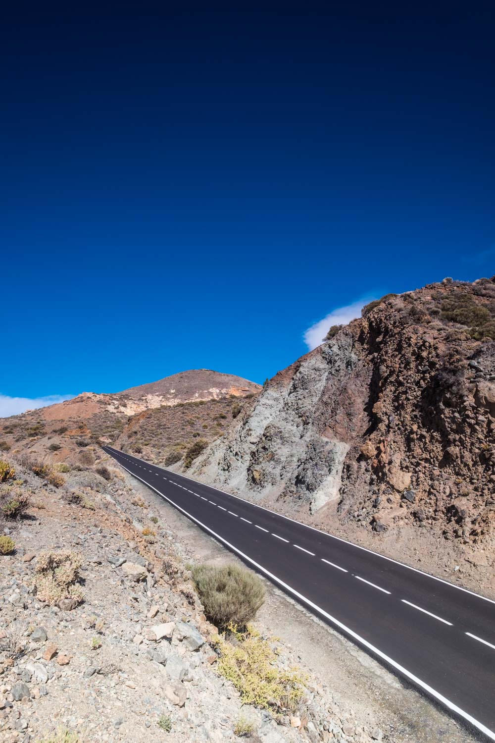 Empty road winding through arid rocky hills under a deep blue sky
