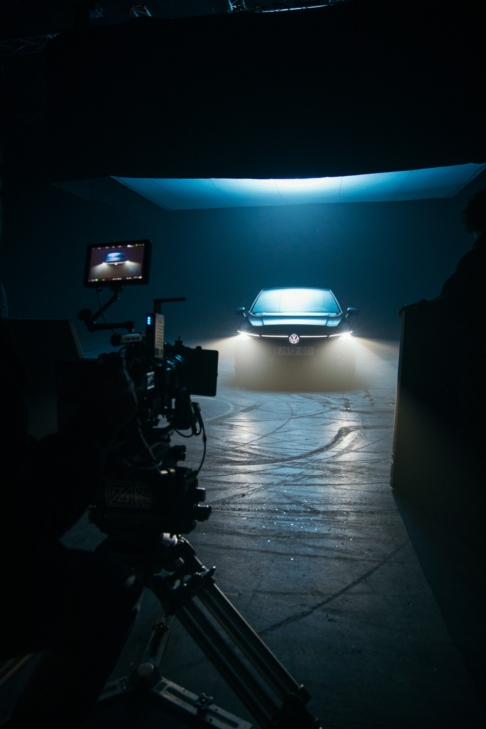 Camera filming a car with its headlights on in a dark studio, on a Glassy Films set