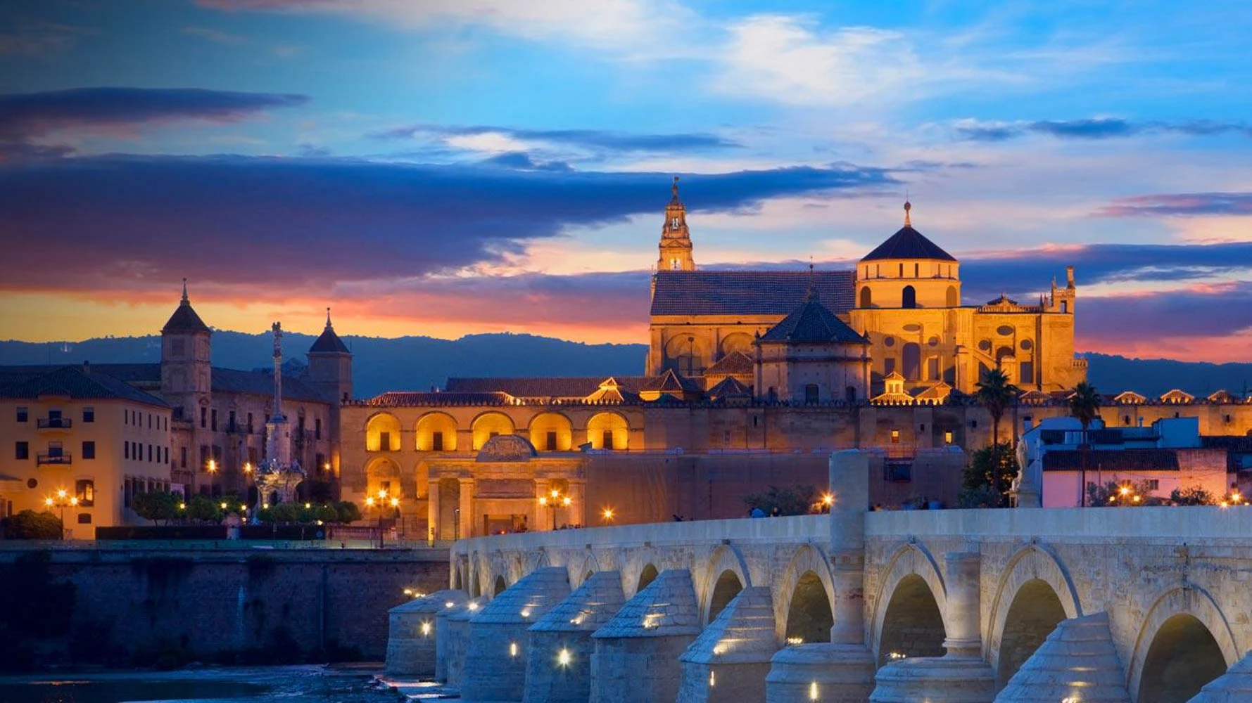The Mosque-Cathedral and Roman bridge of Córdoba lit up at dusk